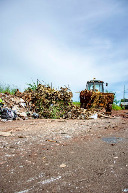 A construction site outside a multi-storey residential building shows a black excavator positioned amidst a heap of rubble composed of broken concrete, bricks, and debris. The excavator's arm is exten