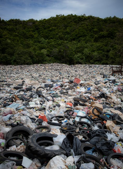 A large pile of mixed waste and rubbish, including plastic bags, packaging materials, and discarded household items, spread across an open area outdoors. The debris is piled up unevenly, with various